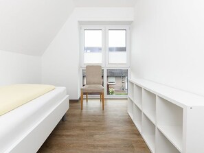 Ein Zimmer mit einem Bett, einem Sessel und einem weißen Regal.