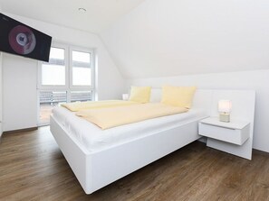 A modern bedroom with a white bed, yellow bedding, a bedside table with a lamp, and a large window.