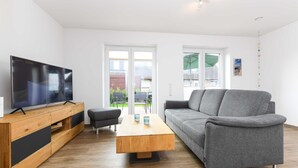 Ein modernes Wohnzimmer mit Couchtisch aus Holz, grauem Sofa und einem Flachbildfernseher auf einem Holz-TV-Schrank.