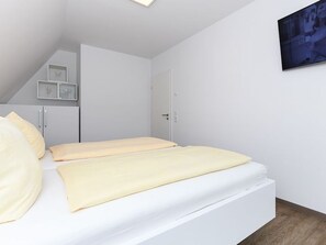 A bedroom with a bed, a wardrobe, a door, and a wall-mounted television.