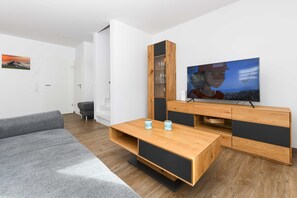 Ein modernes Wohnzimmer mit grauem Sofa, einer Holz-Unterhaltungseinheit und einem Flachbildfernseher.