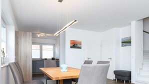Ein moderner Essbereich mit einem Holztisch und vier grauen Stühlen, im Hintergrund eine Küche und eine Treppe rechts.