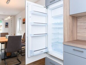 Eine moderne Küche mit integriertem Kühlschrank, einem Essbereich mit Tisch und Stühlen sowie einem Holzschrank.