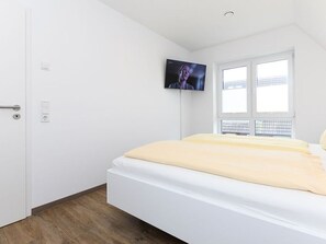 A bedroom with a bed, a television mounted on the wall, a window, and a door. - Licht Vacation Cottage, Germany (Dornum)