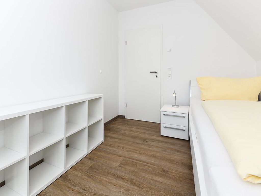 A bedroom with a white bed, a nightstand, a white wardrobe, and a wooden floor.