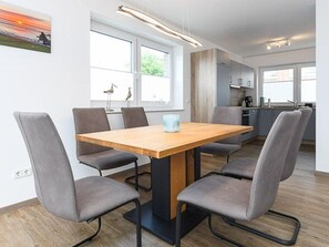 A modern dining area with a wooden table and grey upholstered chairs. - Licht Vacation Cottage, Germany (Dornum)