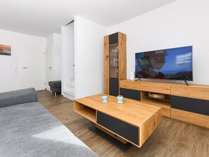 Ein modernes Wohnzimmer mit einer Holz-Unterhaltungsecke, einem Flachbildfernseher und einem grauen Sofa.