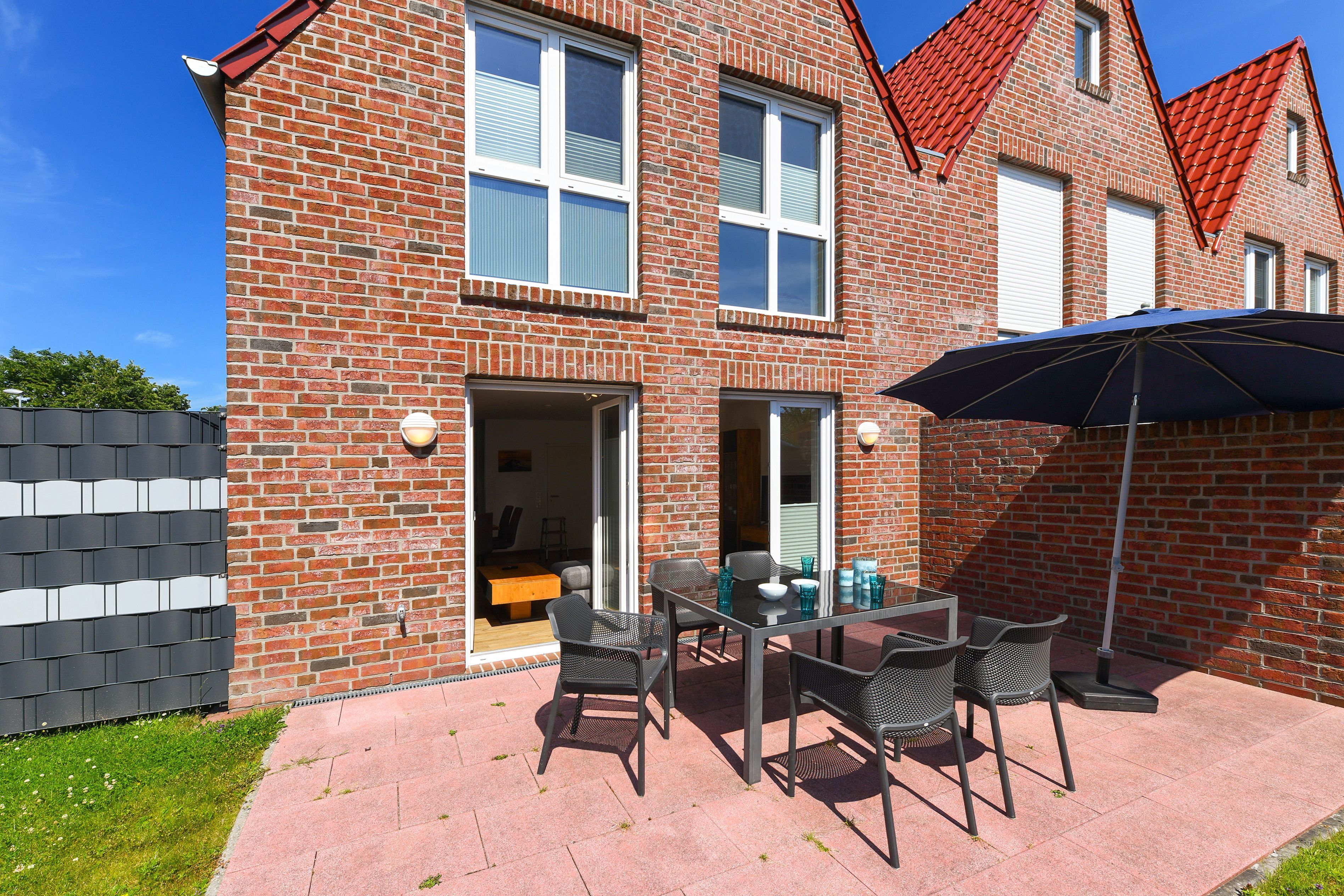 Et murstenshus med en patio med et bord og stole, en skydedør og et rødt tegltag.
