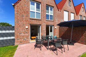 A brick house with a patio area featuring a table and chairs, a sliding glass door, and a red-tiled roof.