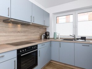 A kitchen with light blue cabinets, a stainless steel range hood, a built-in oven, and a window with blinds. - Licht Vacation Cottage, Germany (Dornum)
