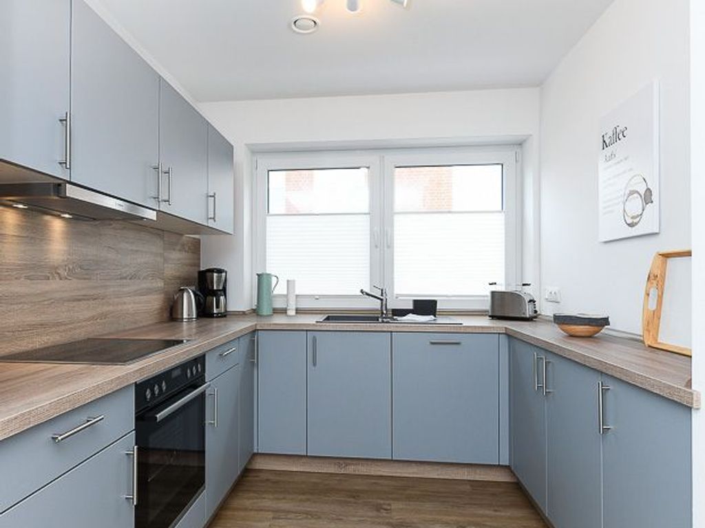 A modern kitchen with grey cabinets, a wooden countertop, and a window with blinds.