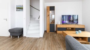 Ein modernes Wohnzimmer mit Treppe, einem grauen Sofa, einem Holztisch und einem Fernseher auf einer Holzkommode.