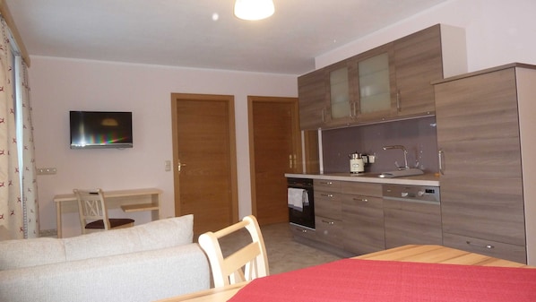 Une chambre de taille modeste comprenant un lit, un téléviseur, un coin cuisine et un espace repas.