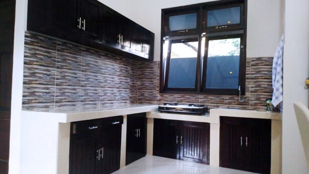 A modern kitchen with dark cabinets, a tiled backsplash, and a window above the sink. - Homestay Purbalingga Tengah Kota by Simply Homy (Purbalingga)