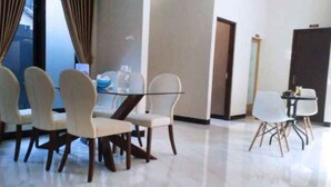 A dining area with a glass table and four chairs, a small table with a chair, and a door in the background. - Homestay Purbalingga Tengah Kota by Simply Homy (Purbalingga)