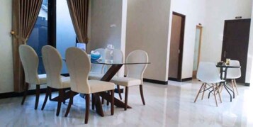 A dining area with a glass table and four chairs, a small table with a chair, and a door in the background.