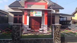 A modern two-story house with a red and beige color scheme, a gated entrance, and a sign for "Simply Home Guest House". - Homestay Purbalingga Tengah Kota by Simply Homy (Purbalingga)