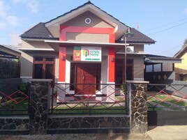 A modern two-story house with a red and beige color scheme, a gated entrance, and a sign for "Simply Home Guest House".
