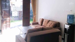 A living room with a sofa, a water dispenser, and a view of a garden. - Homestay Purbalingga Tengah Kota by Simply Homy (Purbalingga)