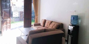 A living room with a sofa, a water dispenser, and a view of a garden.