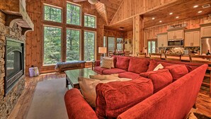 Un amplio salón con un sofá rojo, una chimenea y ventanas grandes que ofrecen vistas al bosque.