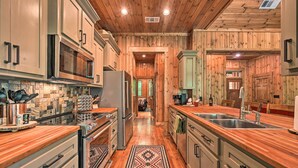 Una cocina con paredes y armarios de madera, electrodomésticos de acero inoxidable y un tapete estampado.
