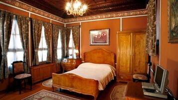 A bedroom with a wooden bed, a desk with a computer, a chair, a wardrobe, and a chandelier.