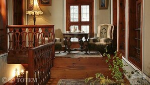 Quarto tradicional com escada de madeira, uma mesa com chaleira, uma cadeira e janela com moldura decorativa.