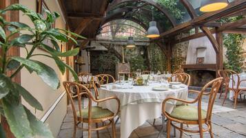 An outdoor dining area with round tables, wicker chairs, and hanging pendant lights.
