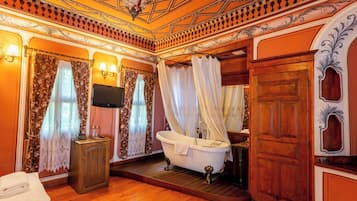 Une pièce avec une baignoire, un plancher en bois, un meuble en bois, une télévision et des rideaux.