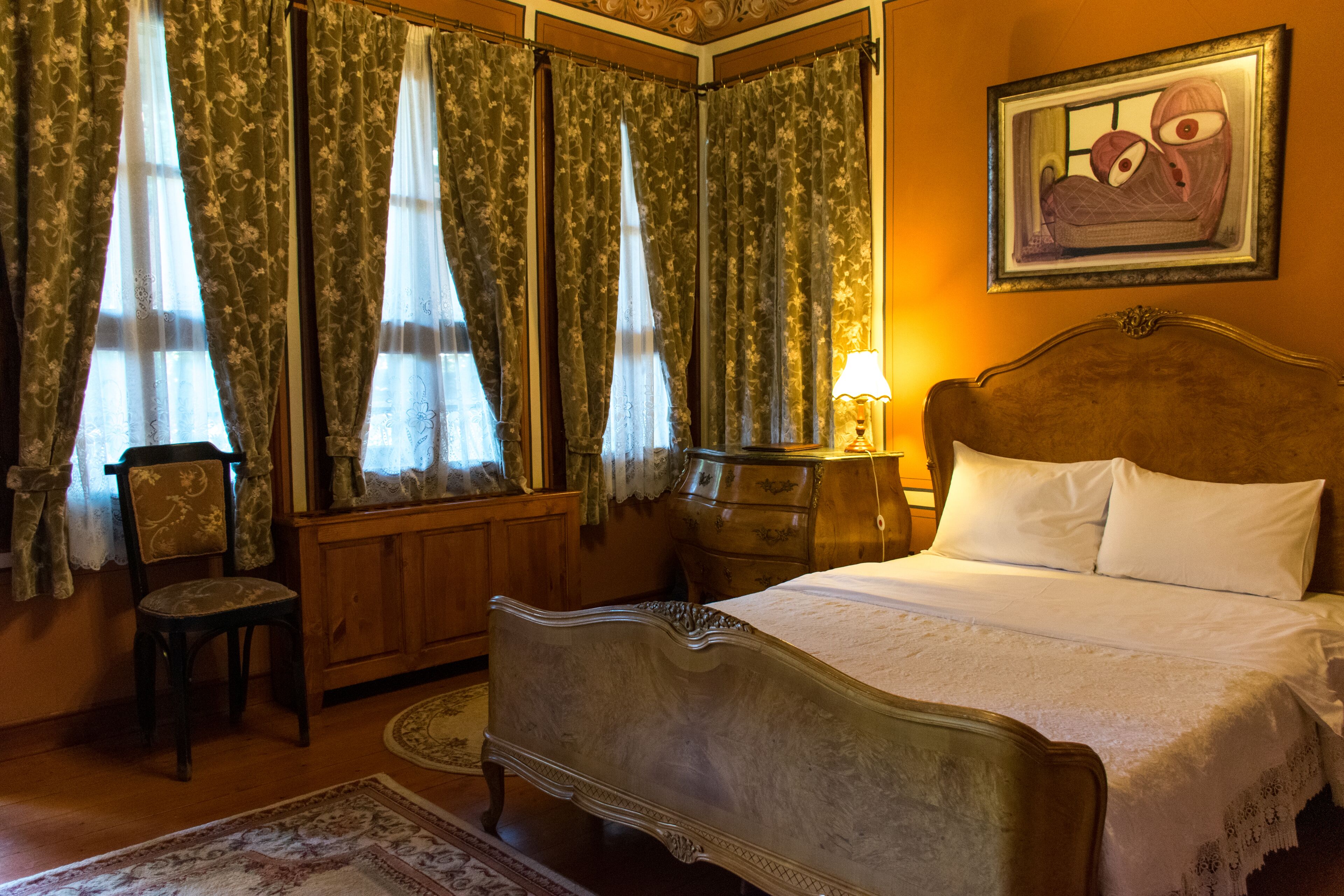 A bedroom with a large bed, wooden headboard, a nightstand, a chair, and curtains.