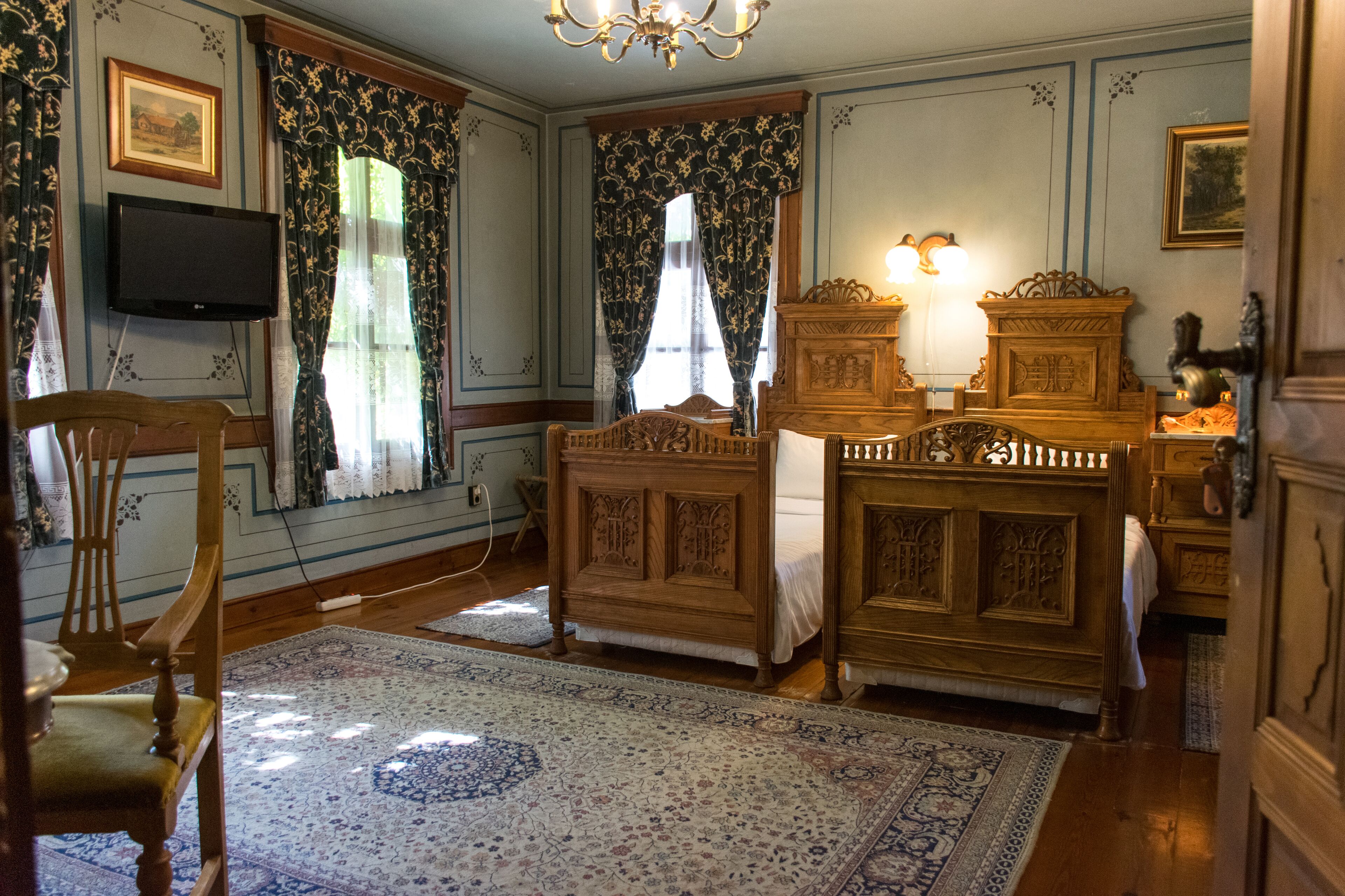 A traditional room with a wooden bed, a wooden dresser, a television mounted on the wall, and a chandelier.