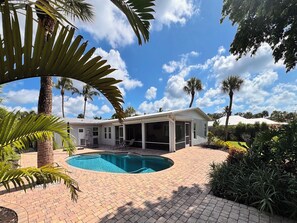 A residential property with a swimming pool, covered patio, and palm trees.