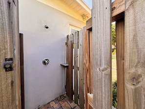 A narrow wooden gate leading to a building with a white exterior wall and a door with a silver handle.