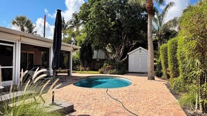 En trädgård med en pool, en täckt uteplats och ett förråd.