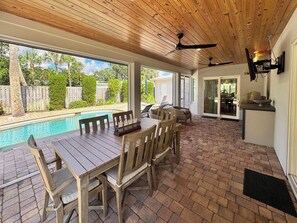 Patio esterno con piscina, mobili in legno e ventilatore a soffitto.