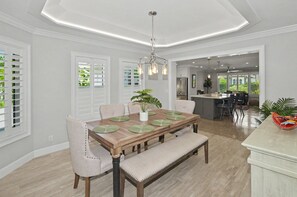 A dining area with a wooden table, chairs, and a bench. There is a kitchen in the background with a refrigerator and a dining table. - Peaceful Paradise Oasis (Stuart)
