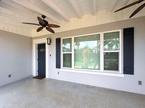Une pièce dotée d’un ventilateur de plafond, de grandes fenêtres avec des volets et d’une porte.