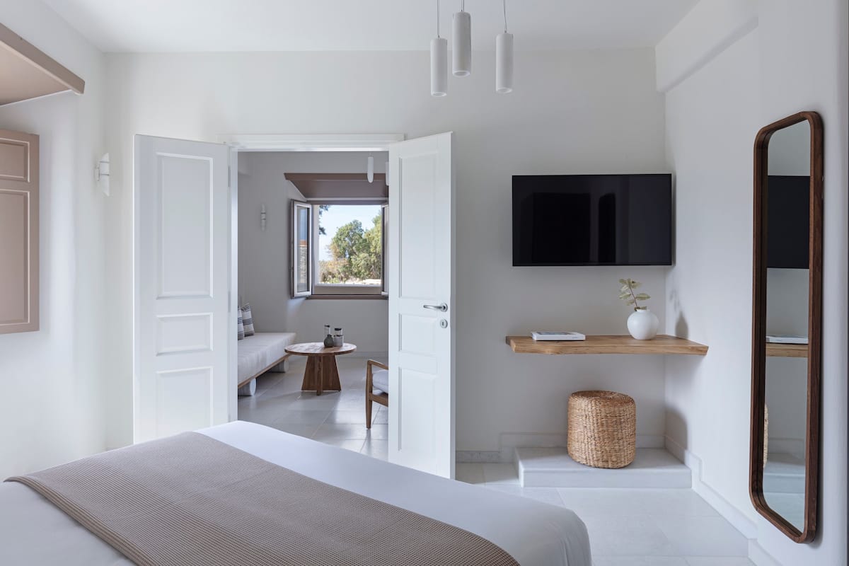 A modern bedroom with a large bed, a mounted TV, a wooden shelf, and a wicker basket.
