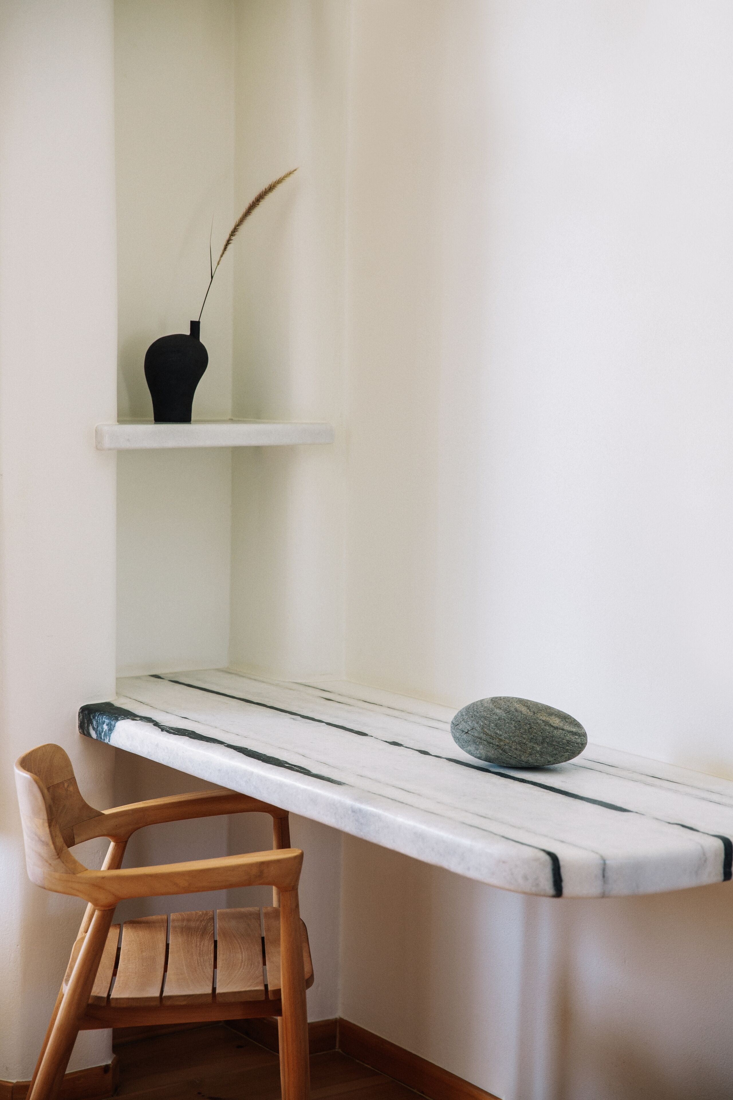 A corner desk with a chair, a vase with a plant, and a stone on the desk.