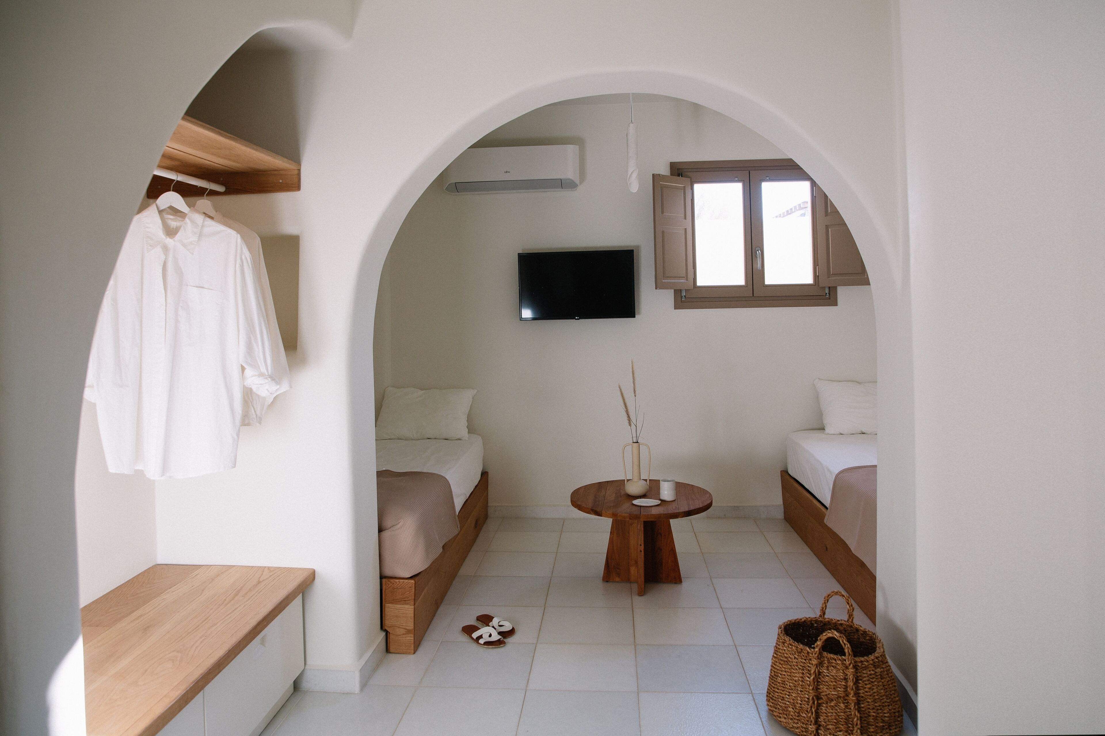 A minimalist room with a bed, a TV, a small table, and a bench.