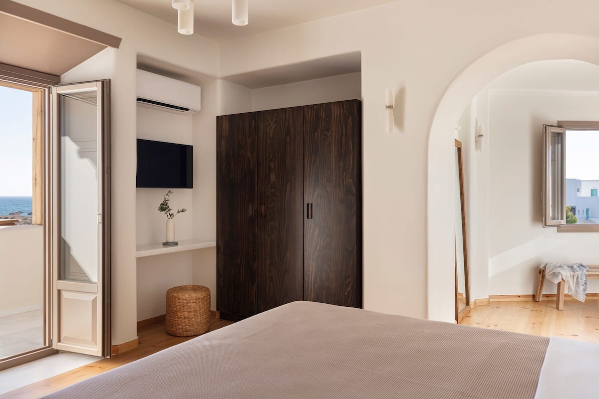 A bedroom with a bed, a wardrobe, a television, and a view of the sea.