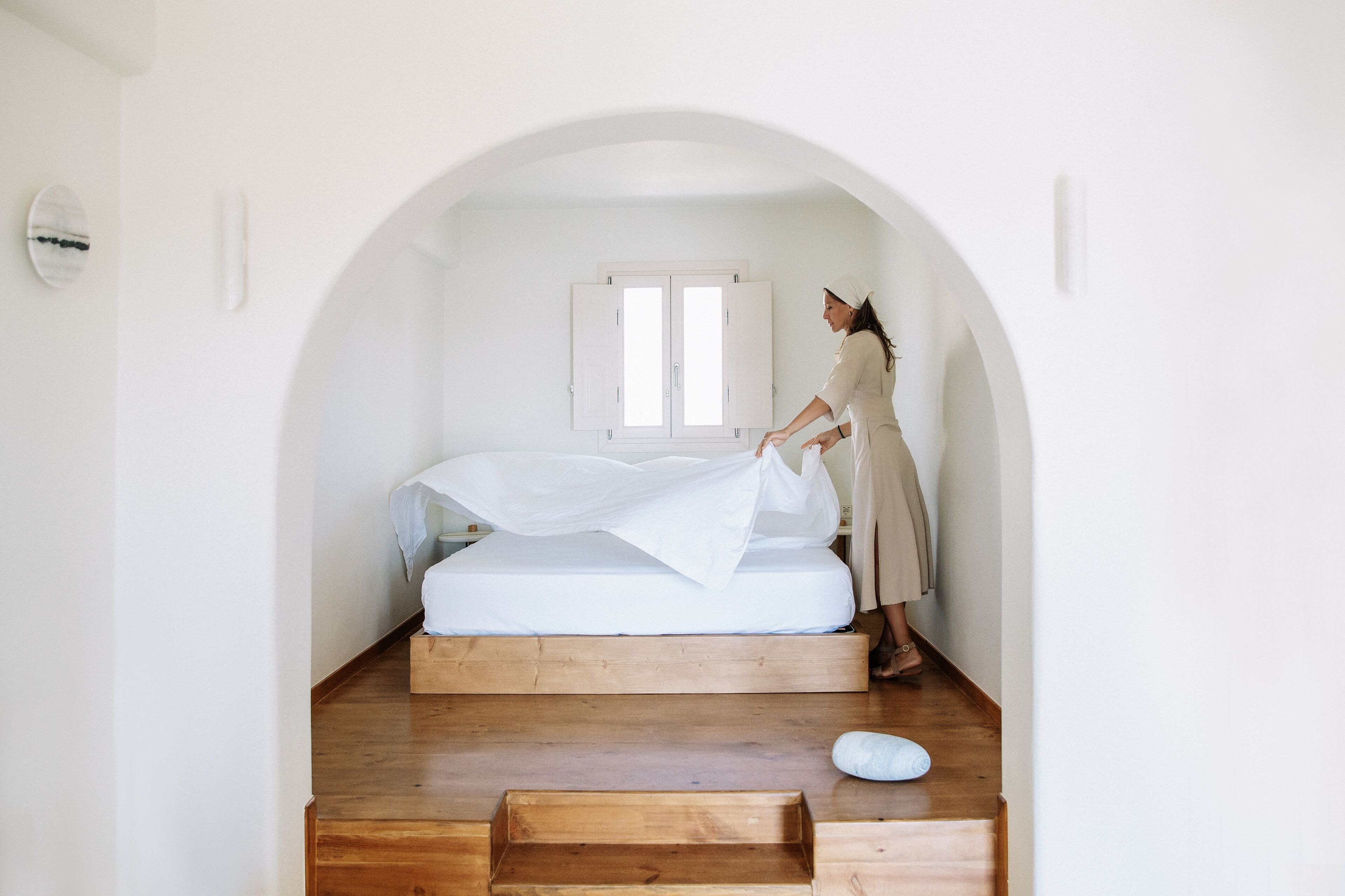 A minimalist bedroom with a wooden platform bed, a white canopy, and a small wooden bench.