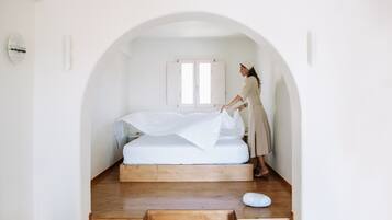 A minimalist bedroom with a wooden platform bed, a white canopy, and a small wooden bench.