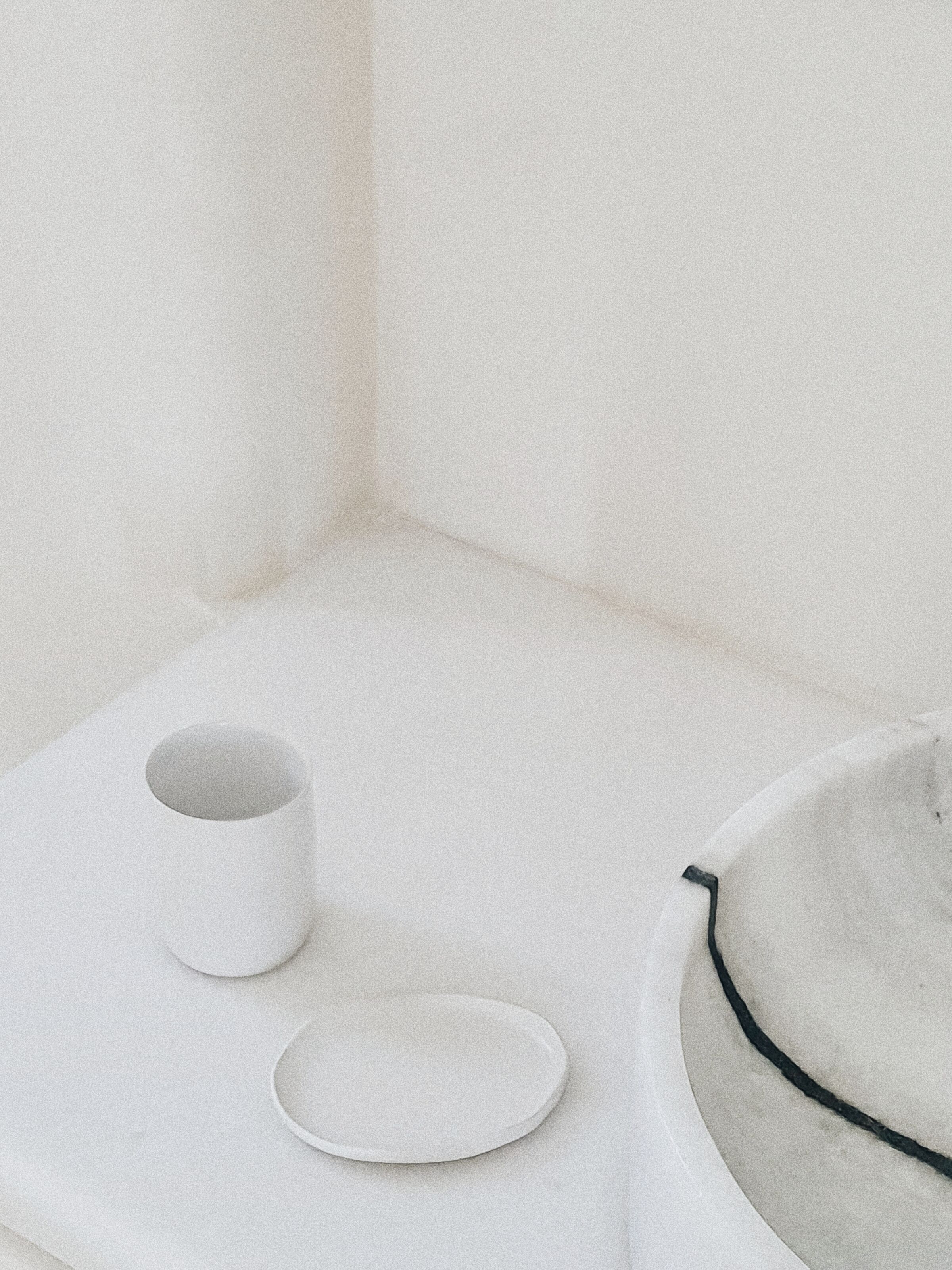Habitació minimalista amb una paret blanca, una taula blanca petita i una cadira blanca amb detall negre.