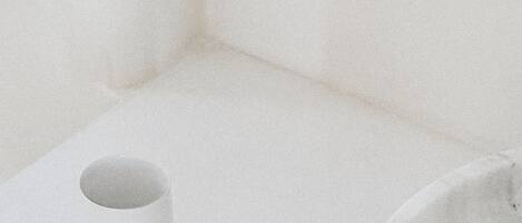 Habitació minimalista amb una paret blanca, una taula blanca petita i una cadira blanca amb detall negre.