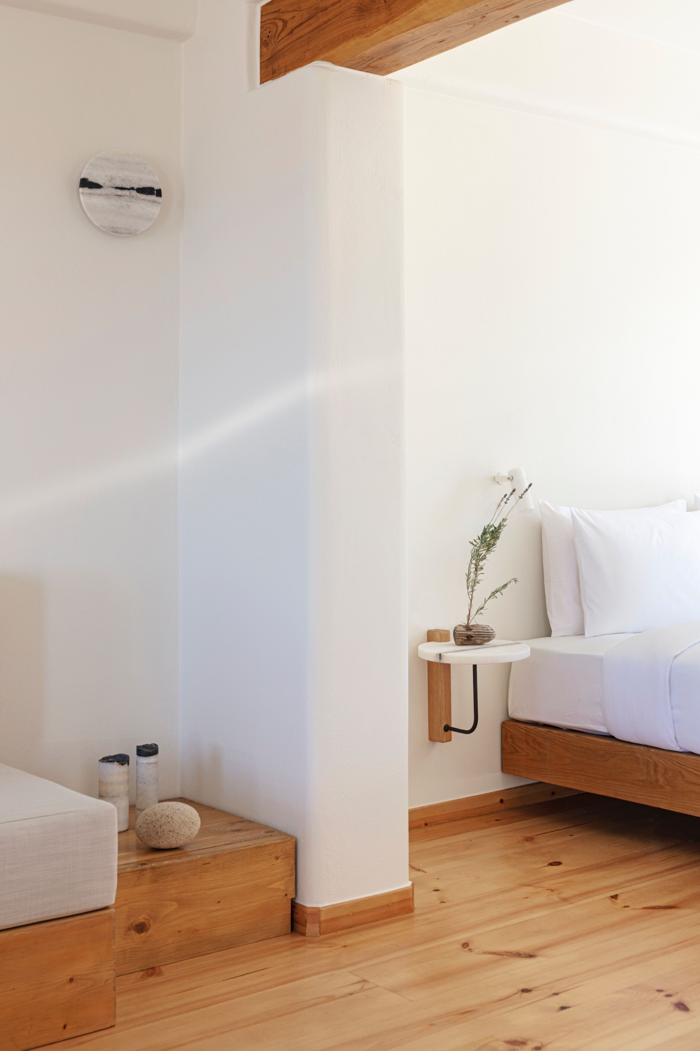 A minimalist bedroom with a wooden bed, a bedside table with a lamp, and a small plant.