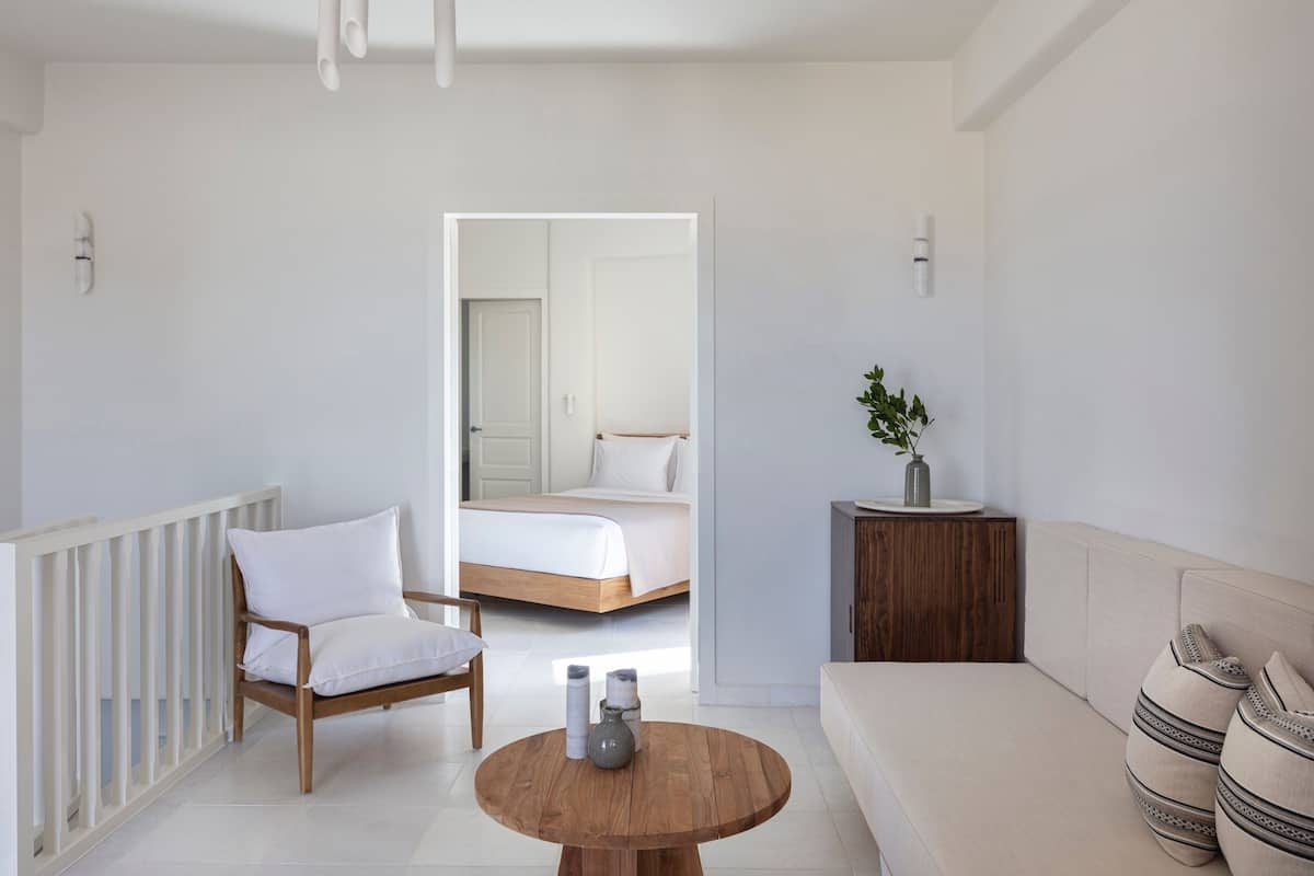 A modern bedroom with a bed, a wooden chair, a round table with bottles, and a sofa.