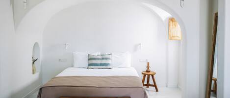 Une chambre avec un grand plafond en arc de cercle, un banc en bois, une table de chevet et un petit tabouret.