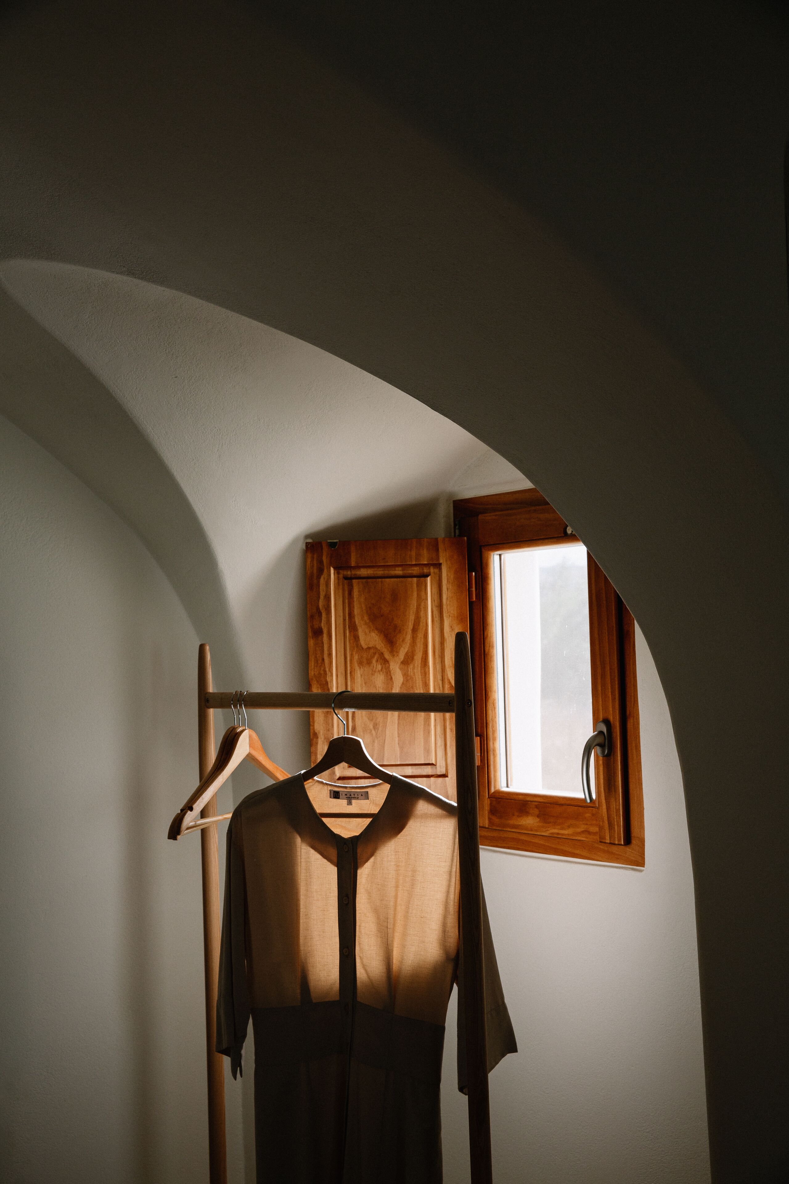 A room with a wooden cabinet, a window, and a clothing rack with a dress.